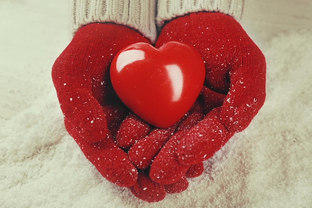 Mains dans des gants rouges chauds tenant le coeur sur fond neigeux