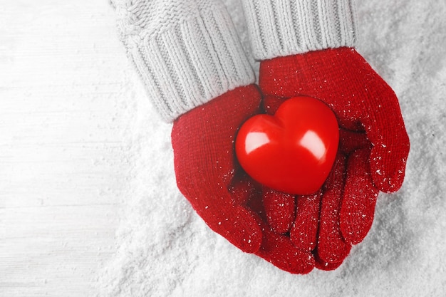 Mains dans des gants rouges chauds tenant le coeur sur fond neigeux