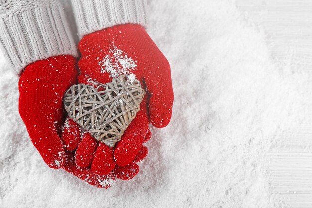 Mains dans des gants rouges chauds tenant un coeur en osier sur fond neigeux