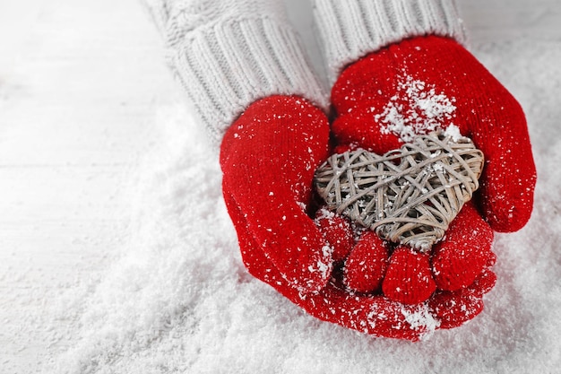 Mains dans des gants rouges chauds tenant un coeur en osier sur fond neigeux