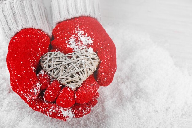 Mains dans des gants rouges chauds tenant un coeur en osier sur fond neigeux