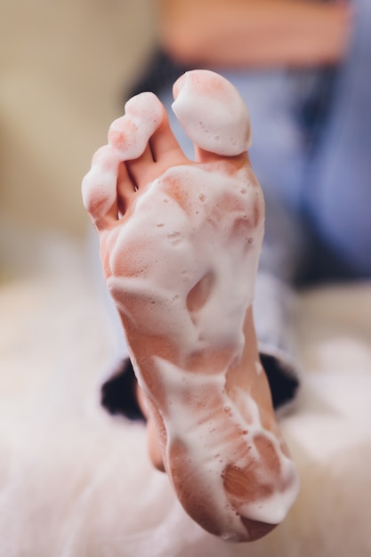 Les mains dans les gants s'occupent des ongles des pieds. Salon de beauté pédicure. Crème hydratante pour les pieds.