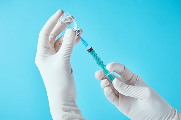 Les mains dans les gants tiennent la seringue d'injection et l'ampoule du flacon de médicament. Concept de soins de santé, médical et de protection contre les virus