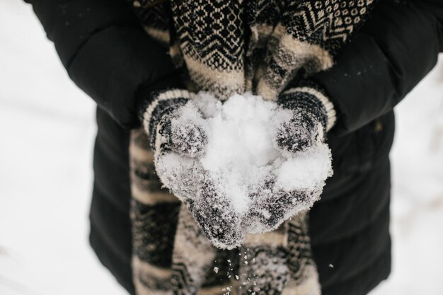 Mains dans des gants tricotés tenant de la neige en gros plan Heure d'hiver jouant des boules de neige Bonheur