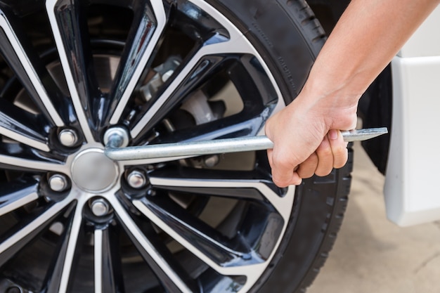 Mains démontant une roue de voiture moderne (jante en acier) avec une clé à ergot pour la roue de changement