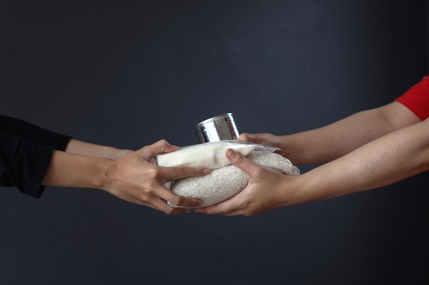 Mains donnant et recevant des aliments de base pour le don et la charité sur fond gris foncé.