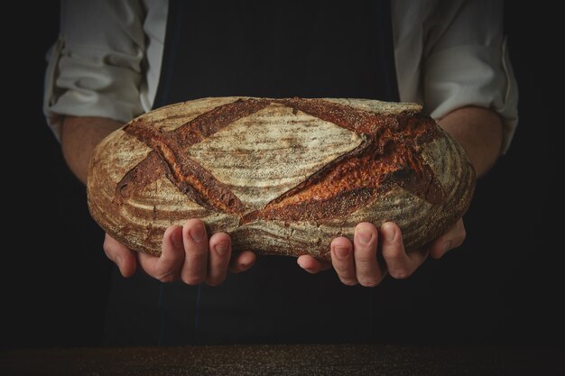 Les mains du boulanger tiennent un pain ovale frais sur un tablier noir