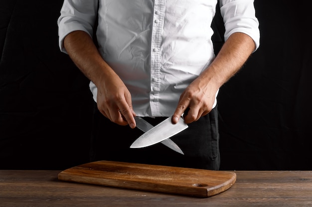 Mains du chef agrandi aiguise un couteau de cuisine sur un couteau