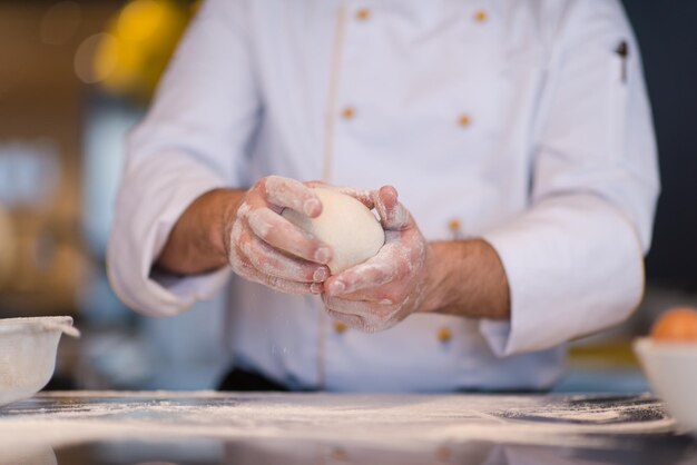 mains du chef préparant la pâte à pizza sur saupoudrée de gros plan de table de farine