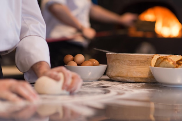 mains du chef préparant la pâte à pizza sur saupoudrée de gros plan de table de farine