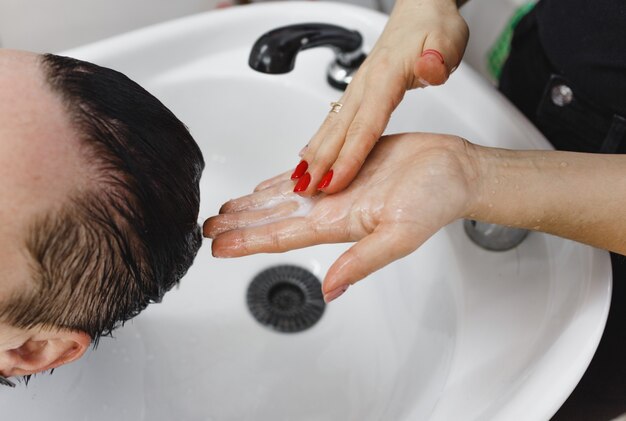 Les mains du coiffeur qui lavent la tête du client en gros plan. Appliquez du shampooing sur vos cheveux.
