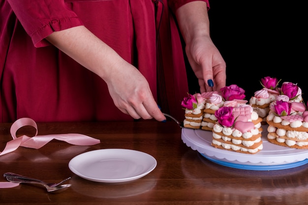 Les mains du confiseur avec un délicat et délicieux gâteau de lettres. Gâteau aux fleurs vivantes, chocolat blanc. Mains d'un pâtissier, emballage de dessert.