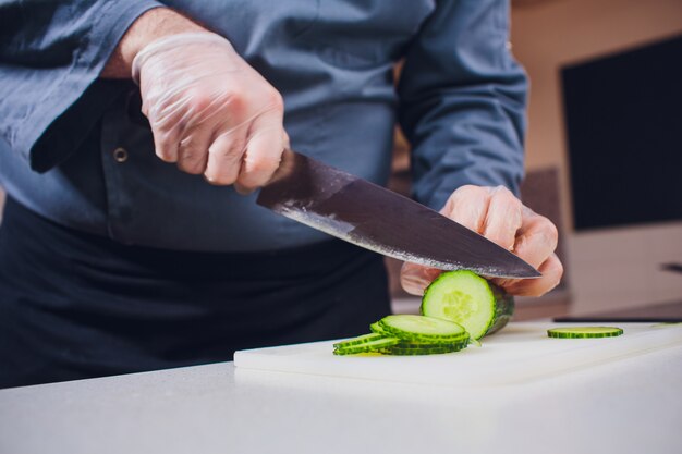 Mains du cuisinier coupant le concombre frais sur planche de bois