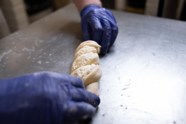 Les mains du cuisinier dans des gants de protection bleus préparent un rouleau farci de fromage cottage et de sucre Production manuelle de produits à base de farine Concept de cuisson et d'ingrédients Place pour le texte