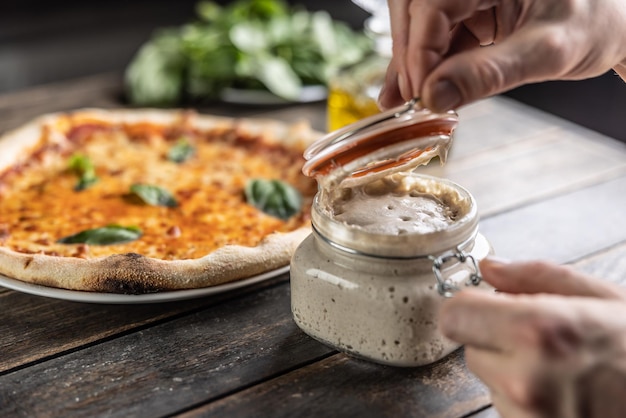 Les mains du cuisinier ouvrent un pot de levain de seigle en arrière-plan une pizza au levain