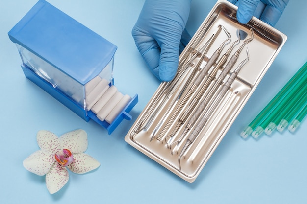 Les mains du dentiste dans des gants en caoutchouc avec un ensemble d'instruments de remplissage composites pour le traitement dentaire dans un plateau en acier sur fond bleu. Concept d'outils médicaux. Vue de dessus.