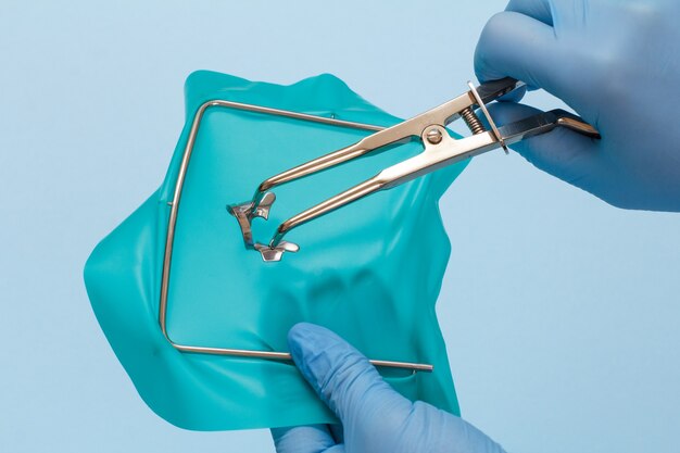 Photo les mains du dentiste dans des gants en latex avec des pinces dentaires, une écharpe de batardeau et un cadre sur fond bleu. concept d'outils médicaux.