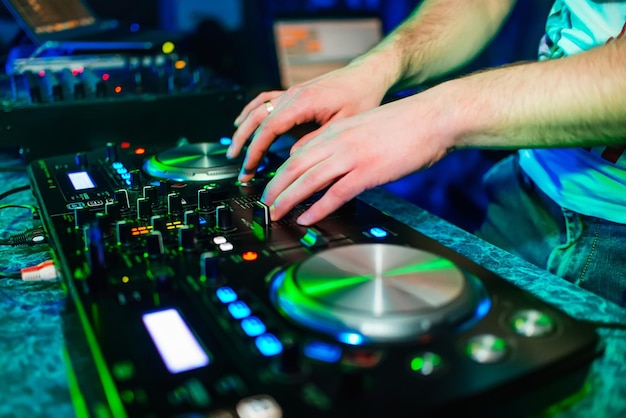 Les mains du DJ mixent de la musique sur une table de mixage professionnelle dans la cabine