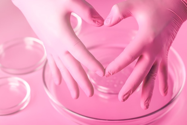 Les mains du docteur dans des gants roses montrent la forme du cœur. Amour et gratitude envers les médecins. Cosmétologie rose.