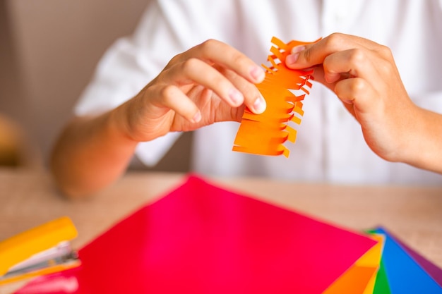 Les mains du garçon coupent l'origami orange avec des ciseaux sur fond de papier gros plan