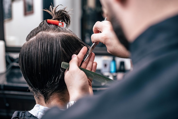 Les mains du jeune coiffeur faisant la coupe de cheveux à l'homme attirant dans le salon de coiffure