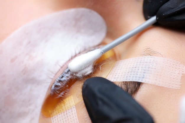 Les mains du maître du laminage des cils avec un coton-tige lissant les cils qui sont collés au rouleau à friser