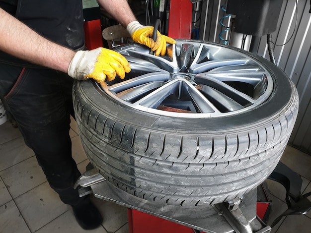 Les mains du mécanicien automobile tenant une roue avec le pneu.