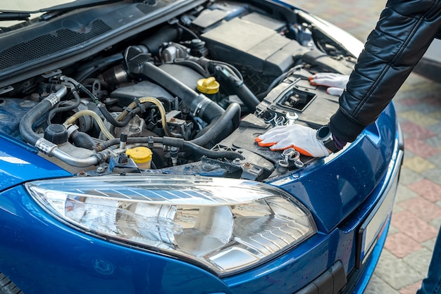 Les mains du mécanicien professionnel dans des gants spéciaux effectuent le contrôle de la voiture sous un capot Concept de réparation de voiture Concept d'inspection de voiture