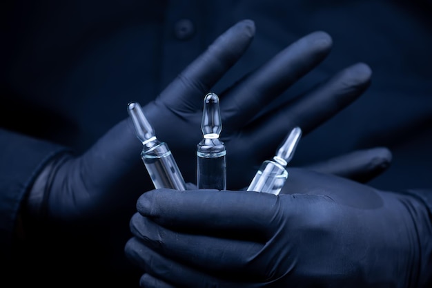 Les mains du médecin dans des gants médicaux noirs tiennent trois flacons de vaccin devant lui