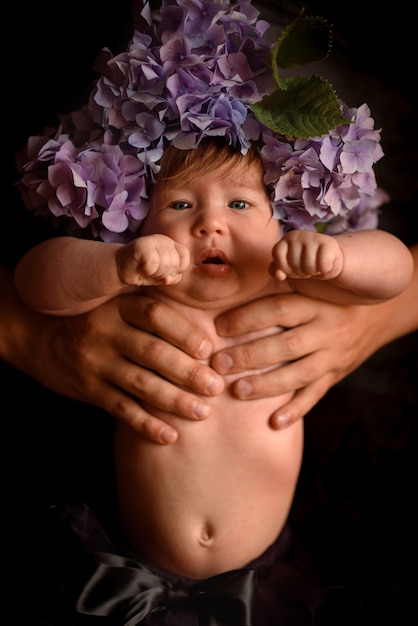 Les mains du père tiennent une petite fille avec des fleurs d'hortensia sur la tête. Tourné dans une pièce noire.