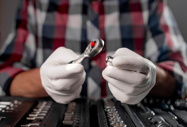 Les mains du réparateur en gants se bouchent avec une poignée à cliquet en acier métallique sur la boîte à outils.