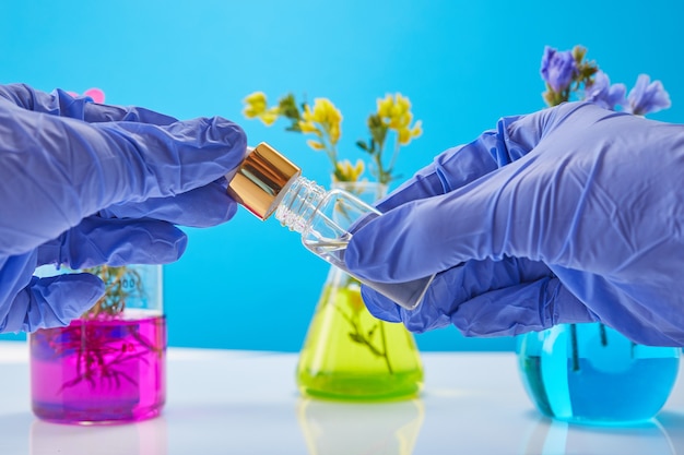 Photo les mains du scientifique tiennent une bouteille de produits cosmétiques, des tubes à essai avec des plantes en arrière-plan.