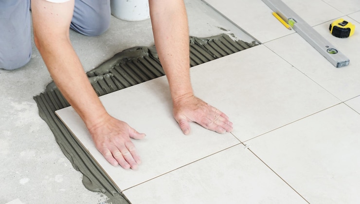 Les mains du travailleur pressent le carreau de céramique au sol.