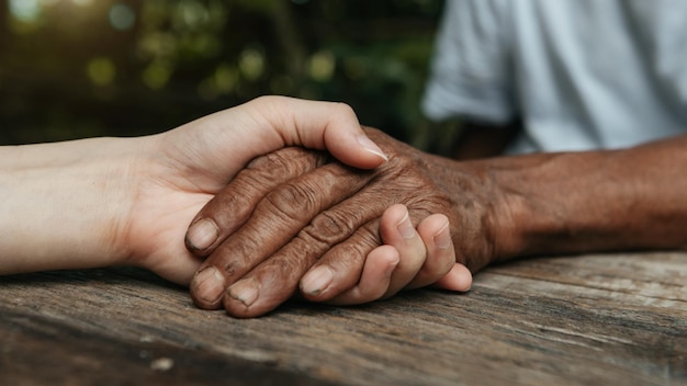 Mains du vieil homme et une main de femme sur la table en bois