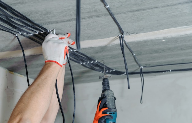 Les mains de l'électricien fixent les câbles électriques au plafond