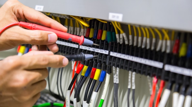 Mains d&#39;électricien testant le courant électrique dans le panneau de commande.