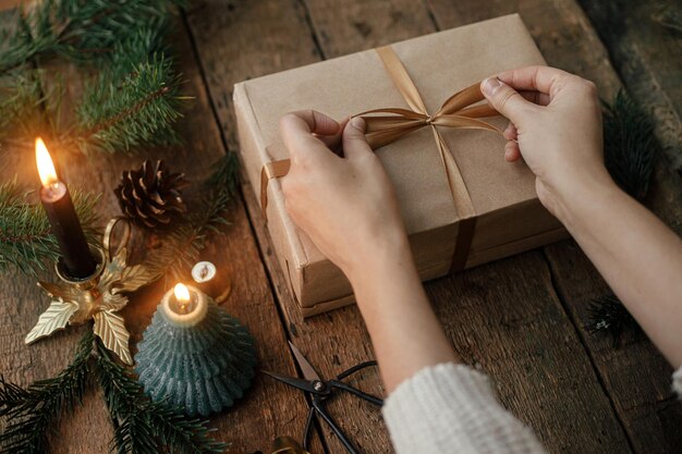 Mains emballant un cadeau de noël élégant dans du papier kraft sur une table rustique Simple cadeau écologique