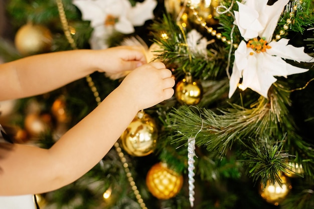 Photo mains d'enfant décorant le sapin de noël avec une boule d'or brillante l'arbre est décoré de guirlandes et de lumières de boules d'argent et d'or de noël