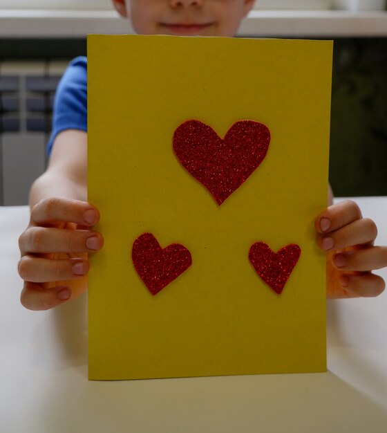 Les mains de l'enfant font une carte à partir d'un coeur en papier agrandi Un cadeau pour la fête des pères