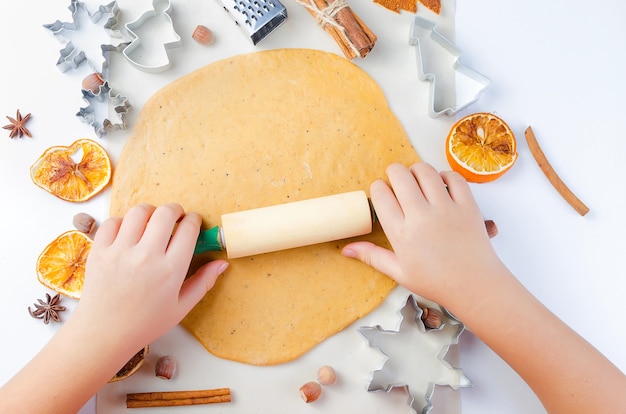 Mains d'un enfant avec rouleau à pâtisserie sur une pâte pour biscuits de pain d'épice de Noël