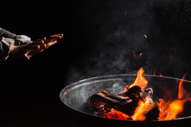 Les mains de l'enfant se réchauffent près du feu du tonneau dans l'obscurité Concept de mendiant émigrant sans-abri