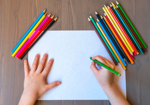 Les mains de l'enfant sont peintes avec des crayons de couleur sur une feuille de papier blanche