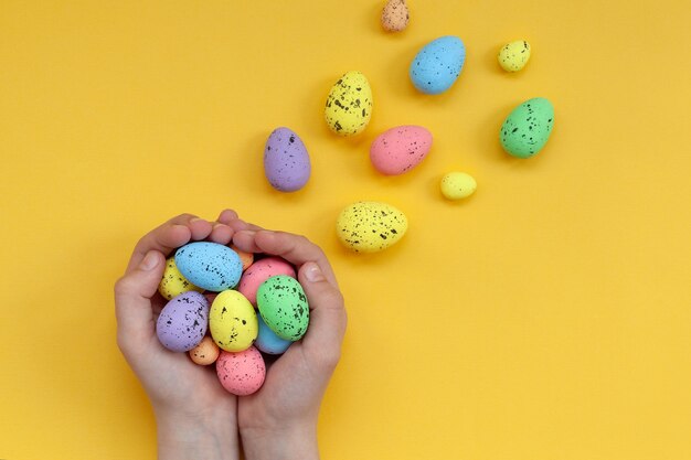 Les mains de l'enfant tenant des oeufs de Pâques peints colorés sur fond jaune. Joyeuses Pâques.