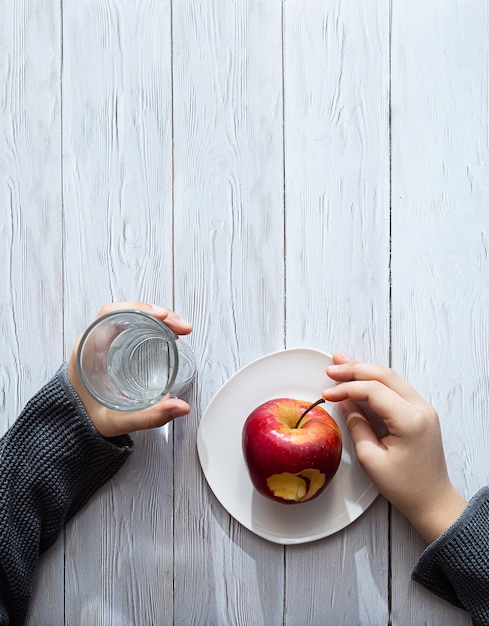 Les mains de l'enfant tiennent une pomme et un verre d'eau