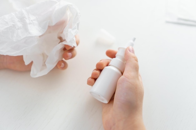 Les mains de l'enfant tiennent un vaporisateur de nez de bouteille et un mouchoir en papier sur fond blanc Traitement du nez qui coule