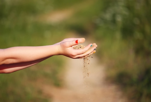 Les mains de l'enfant versant le sable sur fond de nature d'été