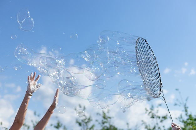 Mains d'enfants attrapant de grandes bulles de savon contre le ciel bleu enfance heureuse