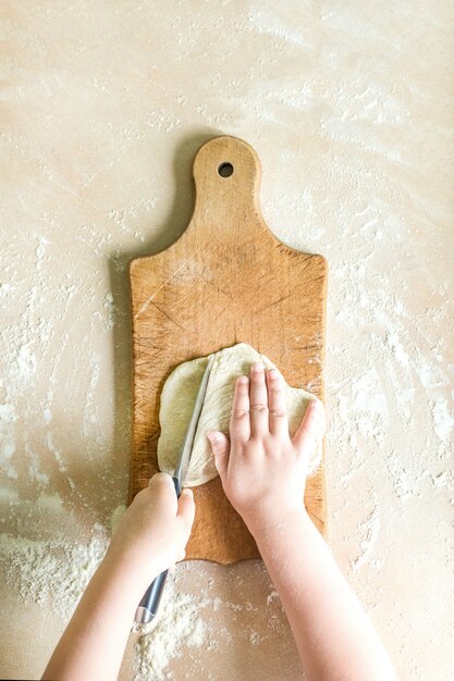 Mains d'enfants coupant la pâte crue