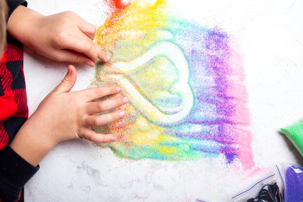 Les mains des enfants créent une forme de cœur avec du sable de couleur arc-en-ciel