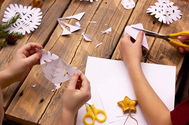Photo les mains des enfants découpent des flocons de neige de papier à la maison sur un fond en bois